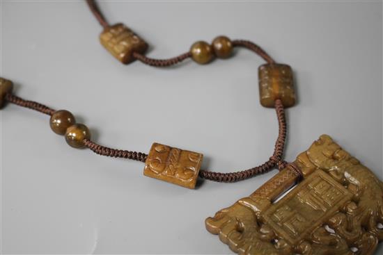 A Chinese hardstone necklace, with carved and inscribed plaque and brown fabric strung beads, plaque 6 x 4.5cm, rectangular beads 2cm a